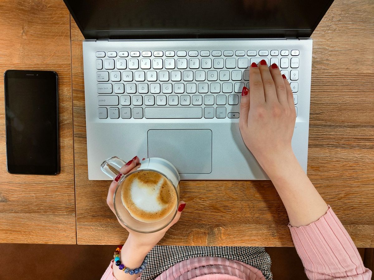 Ung voksen skriver på laptop med kaffekopp ved siden av